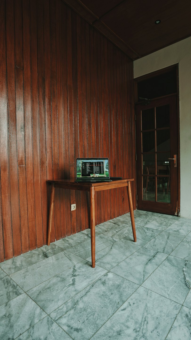 An open laptop displaying code sits on a wooden table.